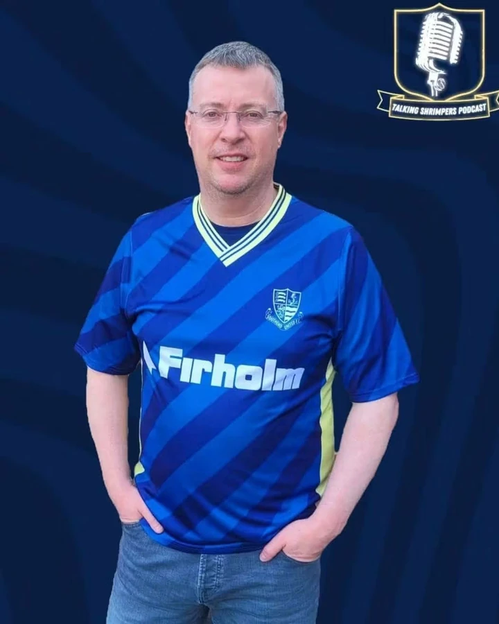 Sensei Phil in a blue Southend shirt against a Talking Shrimpers backdrop.