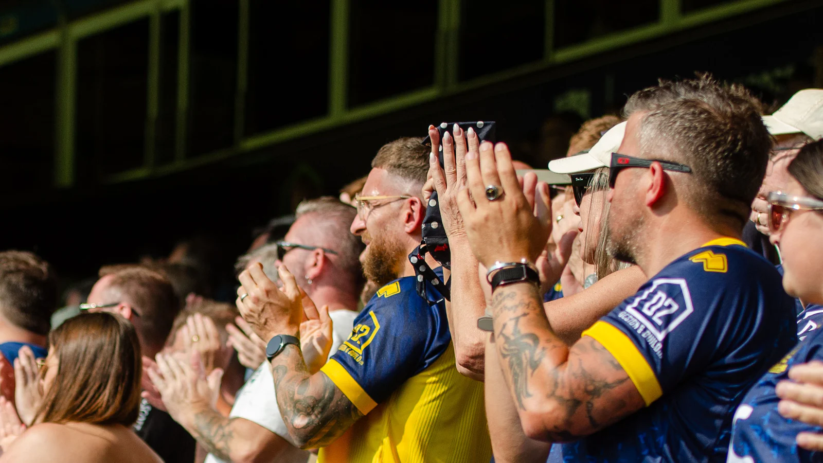 Southend United supporters in navy and gold applauding from the stands at Roots Hall.