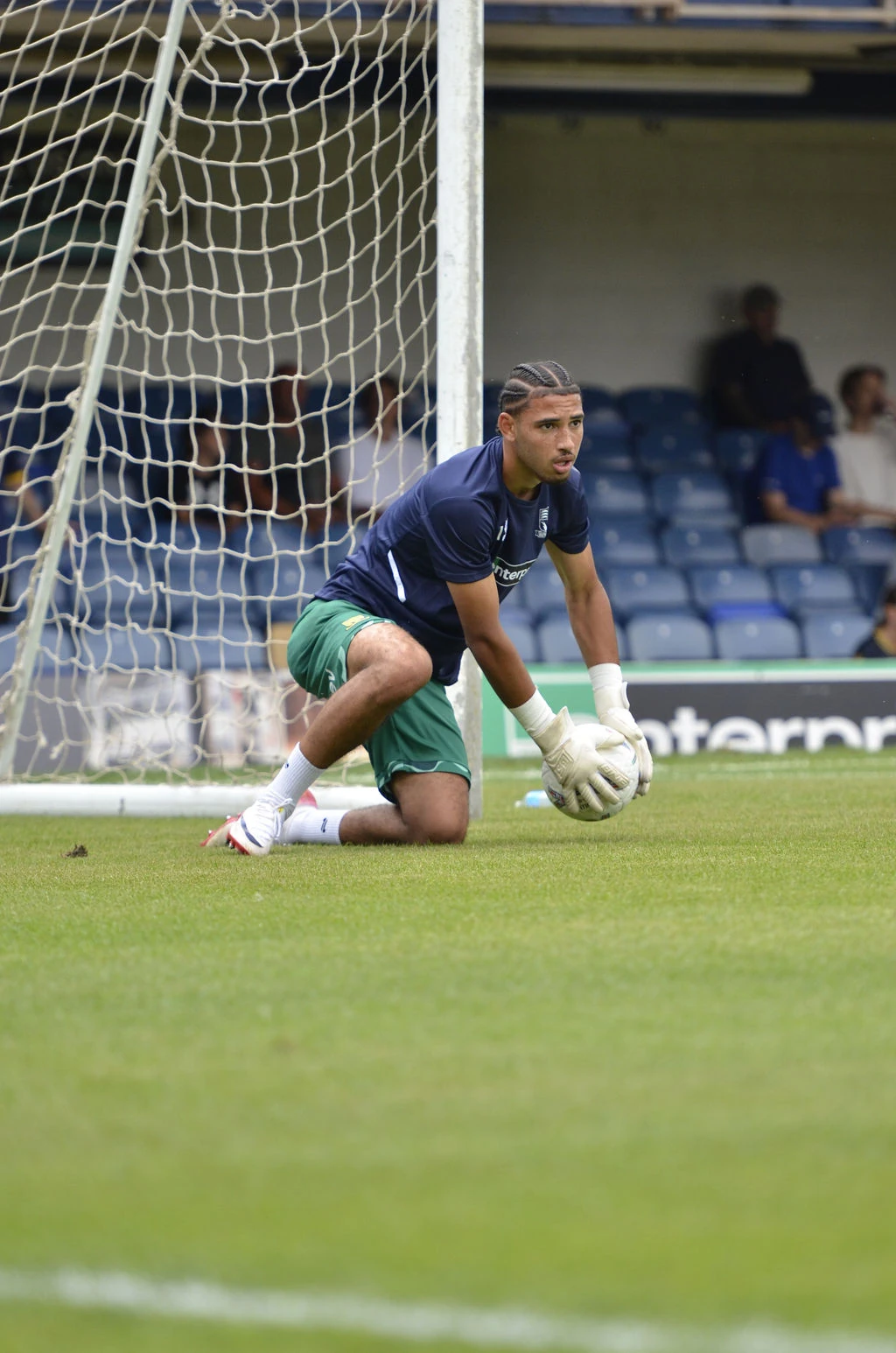 Southend goalkeeper kneels holding the ball during the warm-up in front of goal.