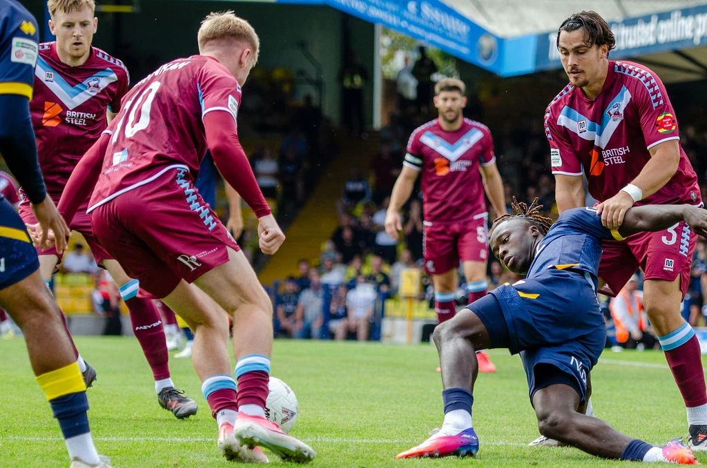Southend attacker lies on the pitch among Scunthorpe defenders as the ball remains loose.