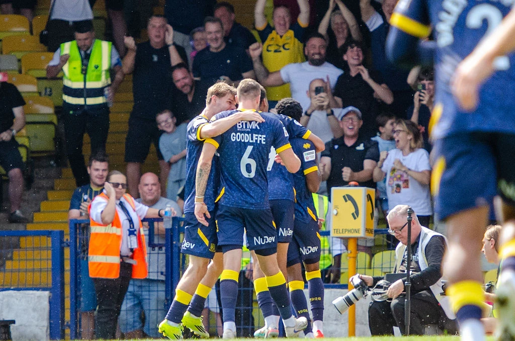 Southend players embrace in celebration in front of Roots Hall supporters.